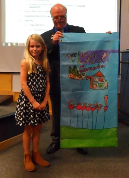 Student holding their winning banner design featuring a colorful maple leaf and "150th Birthday"