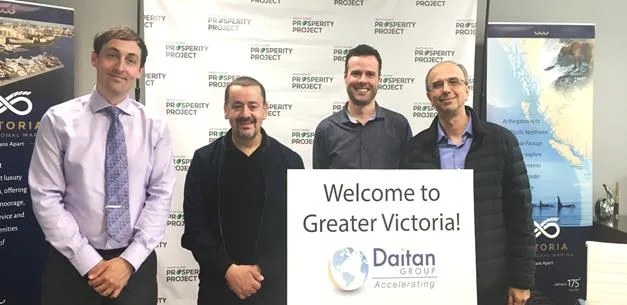 Four men standing in an office holding a "Welcome to Greater Victoria! Daitan Group Accelerating" sign