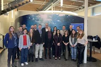 Group photo of approximately 15 people standing in the COAST hub office