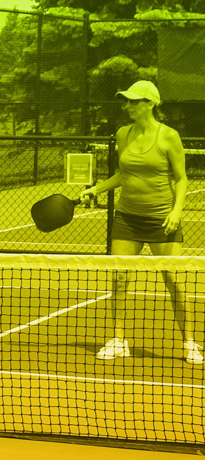 Woman in visor and grey tank top ready with a pickleball paddle at the net