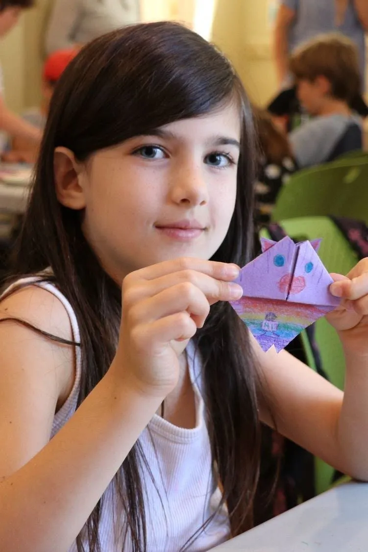 Photo of a young girl holding up a purple origami craft she made.