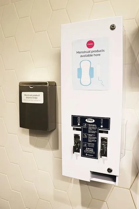 Photo of a wall-mounted dispenser providing free menstrual products in a restroom.