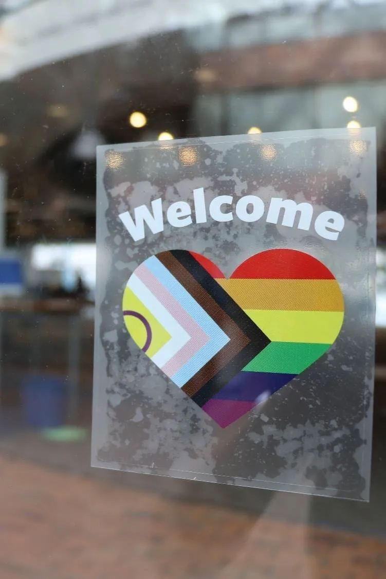 Photo of a window sticker with a Progress Pride heart and the word "Welcome."