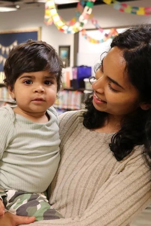 Photo of a woman smiling while holding a young child in the library.