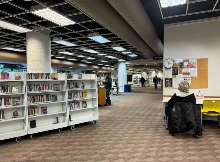 Photo of a person browsing books on white mobile shelving units in a library aisle.