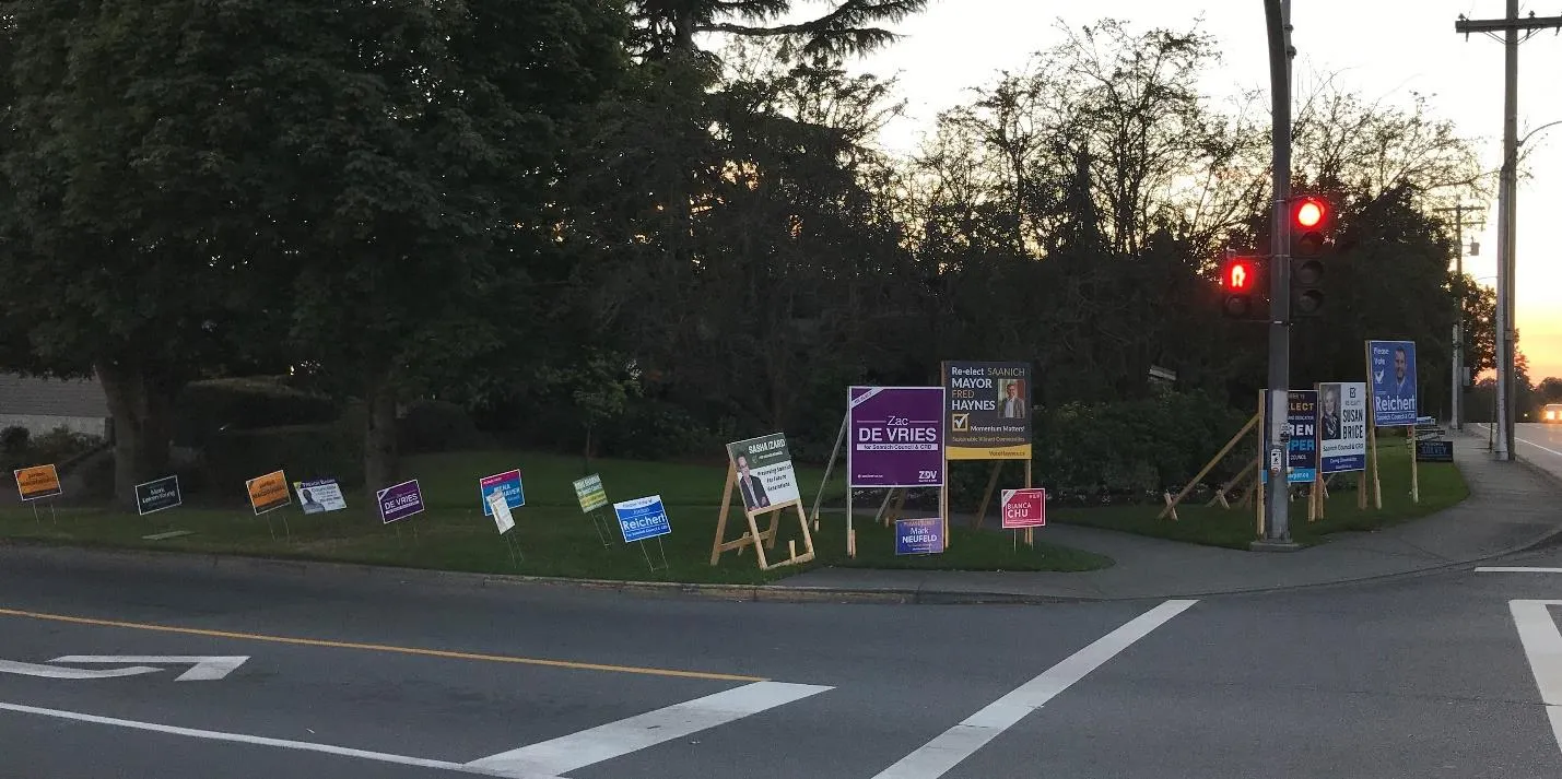 Panorama of numerous election signs for multiple candidates at a busy street intersection at dusk