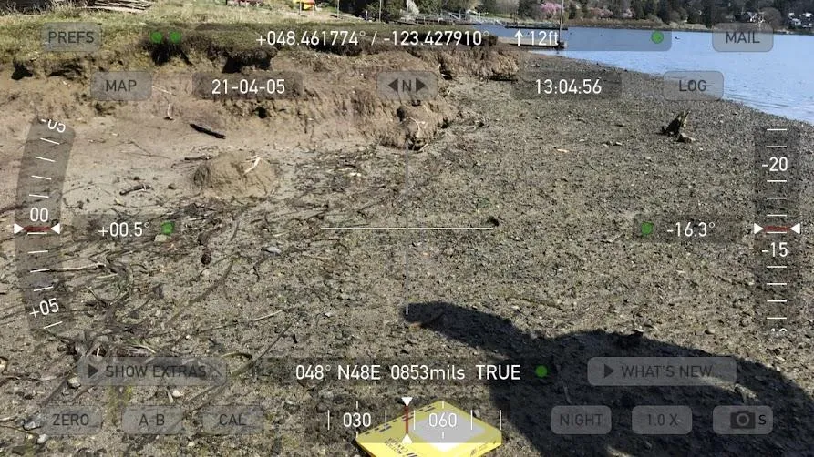 Photo of a muddy, sparsely vegetated intertidal area with a camera overlay showing coordinates (+048.461774 / -123.427910), the date (21-04-05), and an elevation of 12ft.