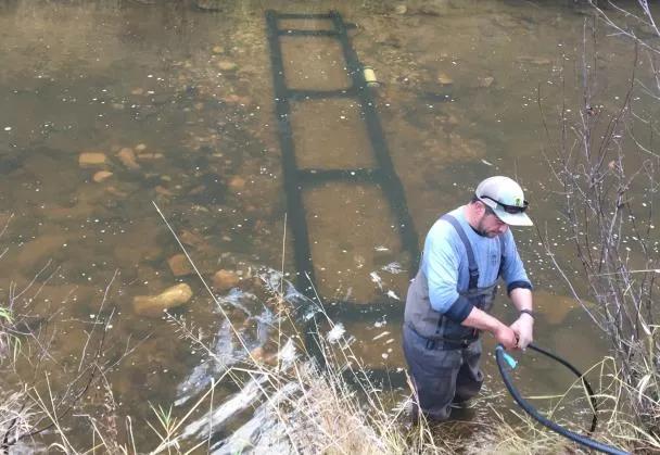Photo of a PIT tag antenna array being installed on the stream bed by a person in waders.