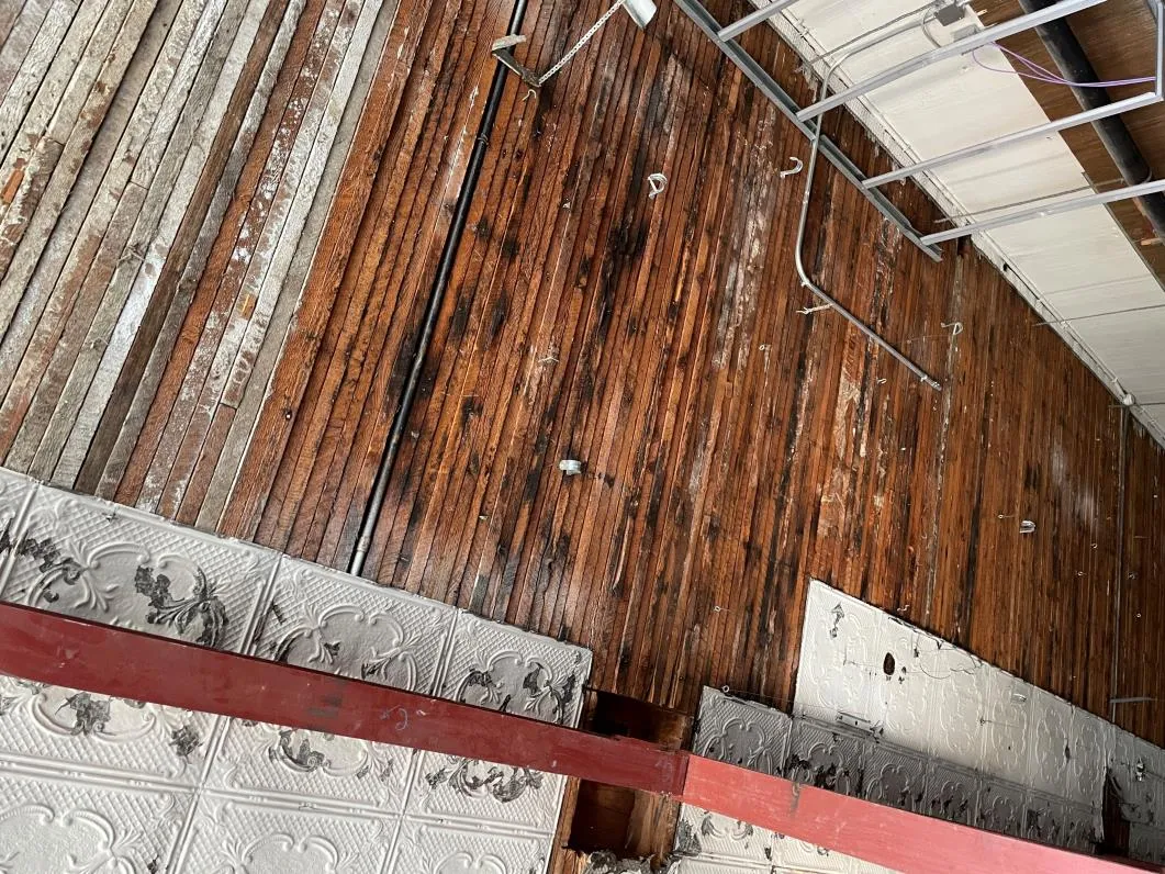 View of an interior ceiling being dismantled, revealing original wood lath and decorative tin ceiling panels