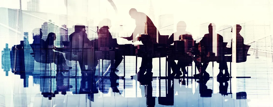 Silhouette of several people sitting around a table in a meeting