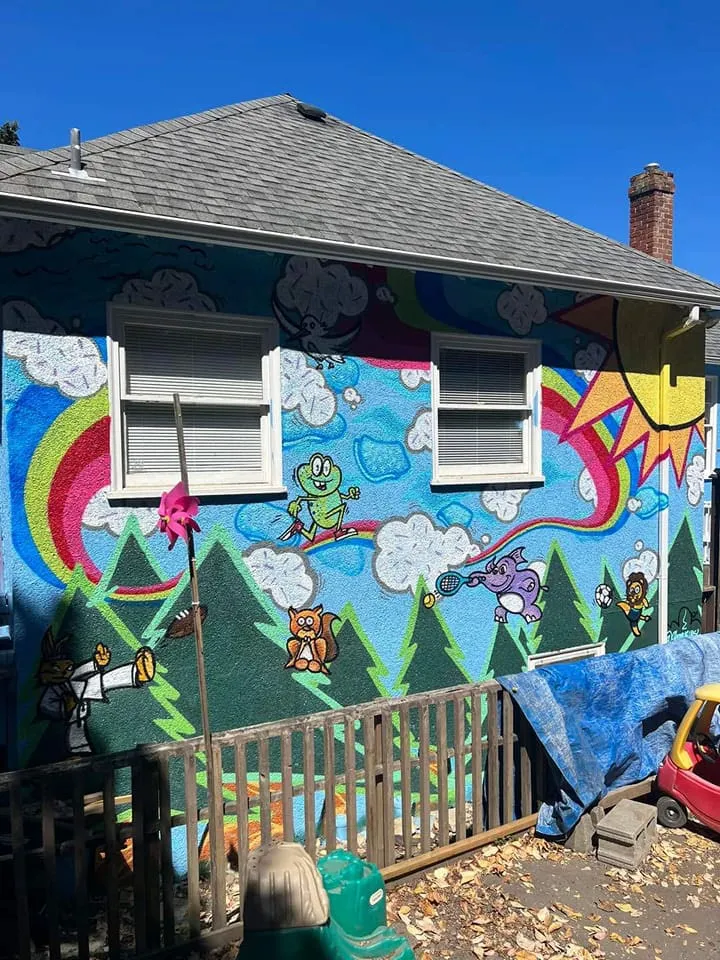 Colorful outdoor mural on a building wall featuring cartoon characters, mountains, and a rainbow