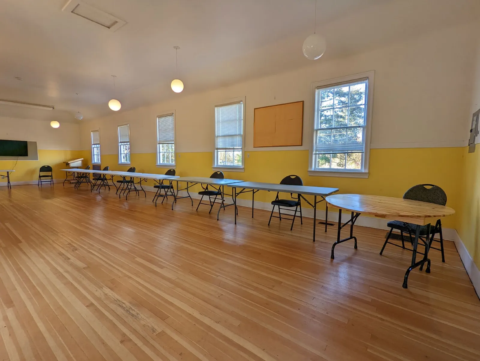 Wide view of the hall interior with wood floors and long tables set with chairs against a yellow and white wall