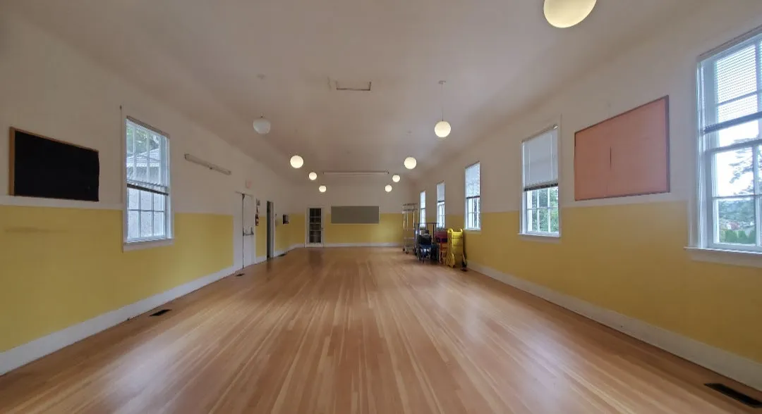 Interior view showing the length of the empty hall with wood flooring and natural light from windows