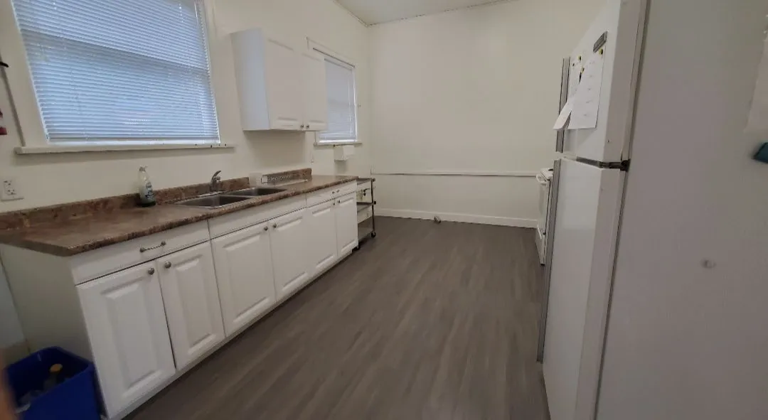 View of the kitchen area with white cabinetry, a sink, and a refrigerator