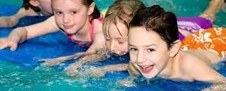 Children playing on a blue float in a swimming pool