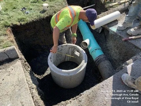 Construction worker installing a catch basin in a trench
