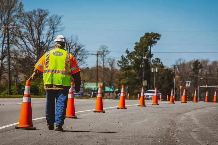 a construction worker in high-visibility gear walking among orange traffic cones on a road