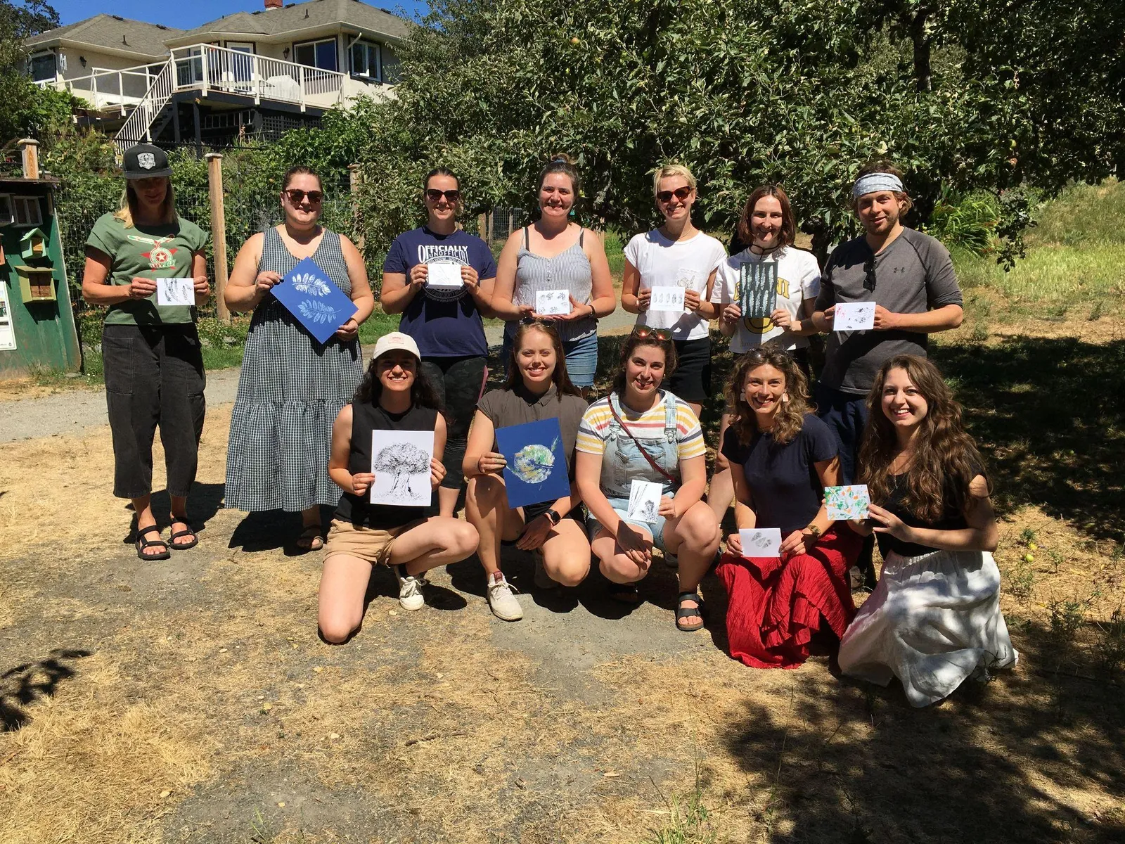 A group of volunteers posing together and holding up small blue and white art prints they created.