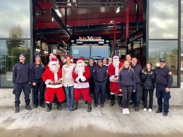 Large group of members and volunteers, including two Santas, in front of the fire hall