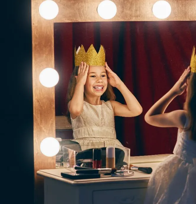 Young girl wearing a gold crown looking into a vanity mirror
