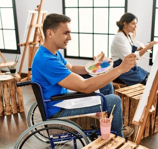 Man in a wheelchair painting on a canvas at an easel