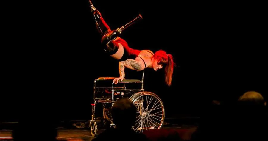 Performer with prosthetic legs performing a handstand on a wheelchair on stage