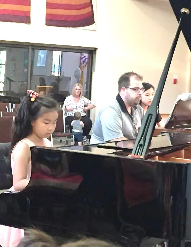 Girl and a teacher playing a grand piano together