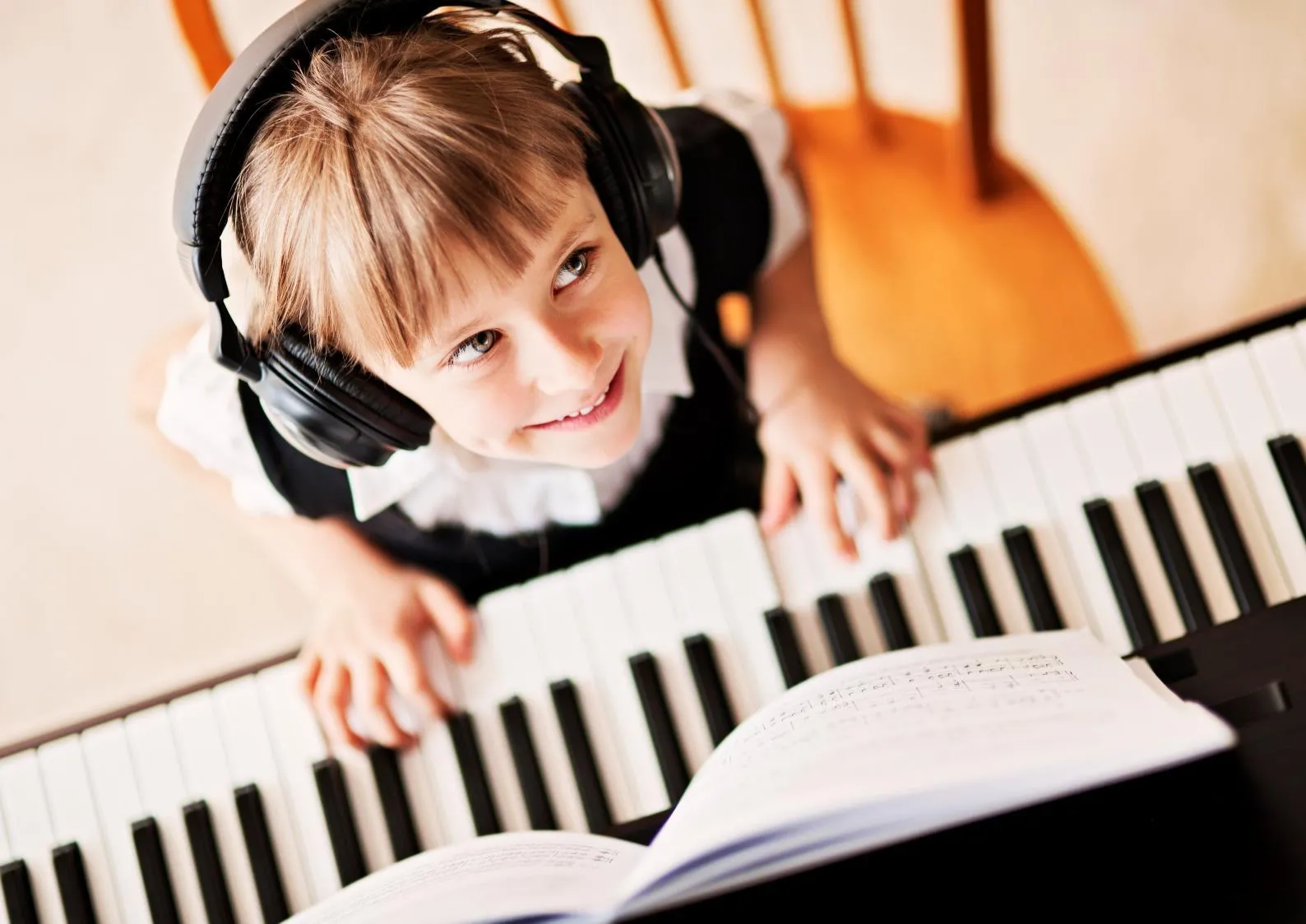 A young girl wearing headphones and smiling while playing a piano