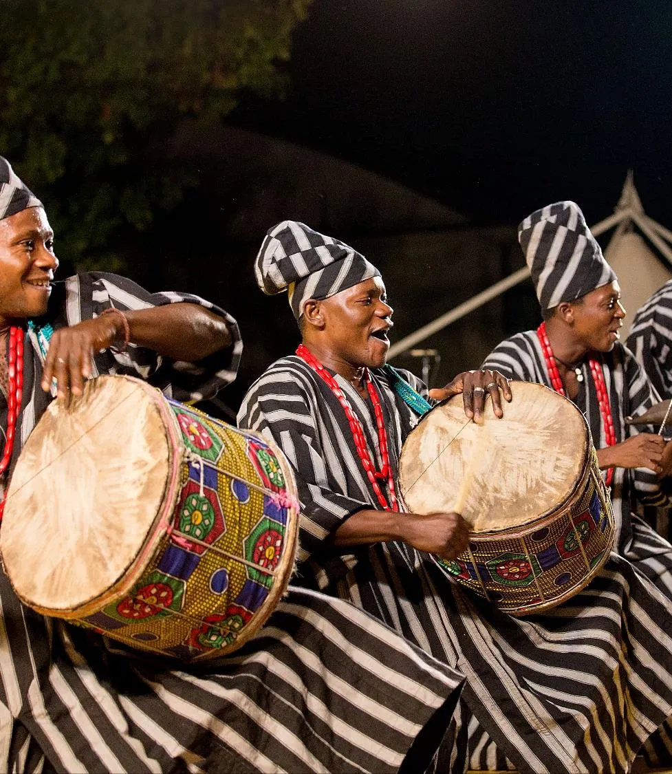 Three men in traditional striped attire playing drums