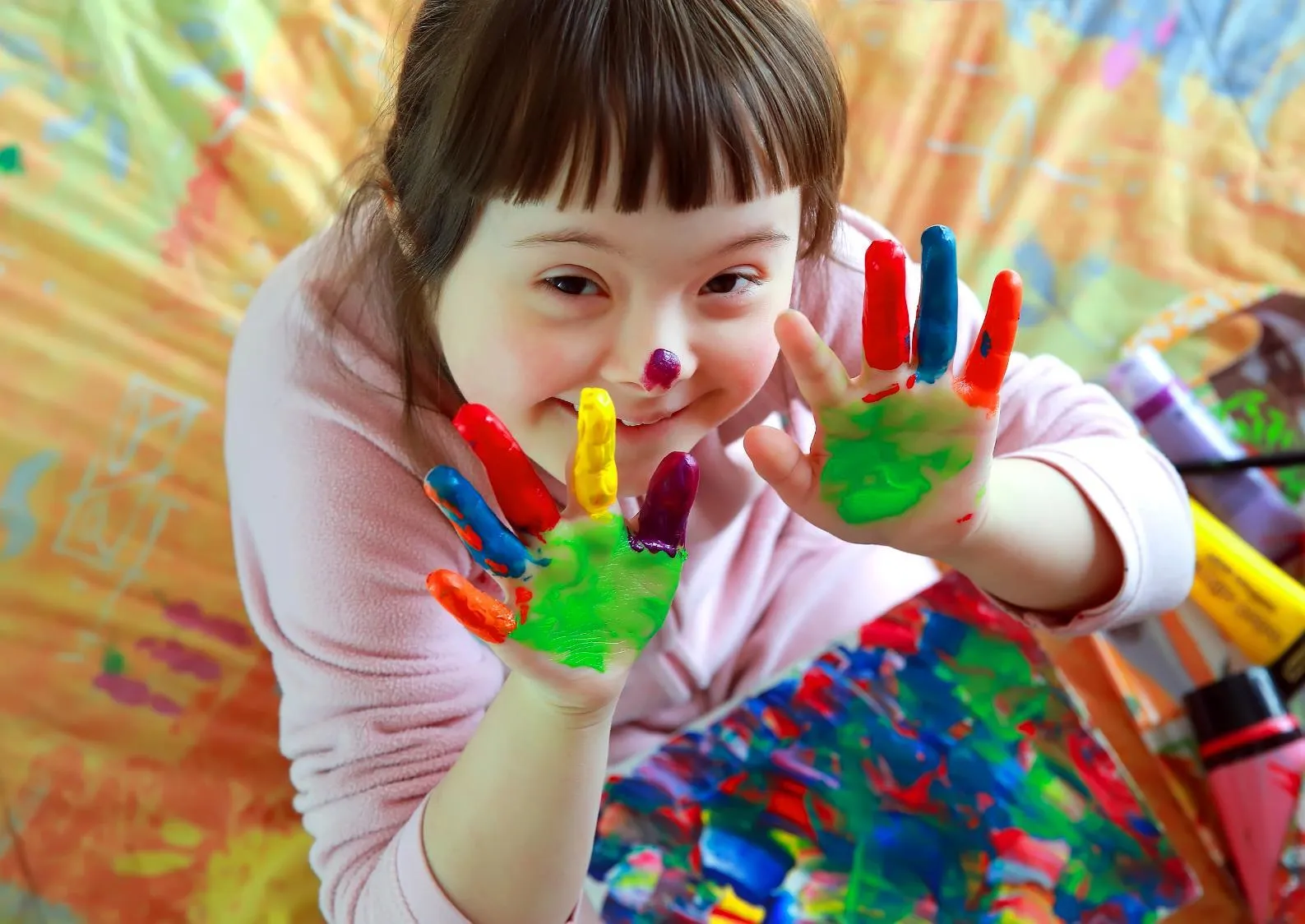A child with colorful paint on their hands and nose