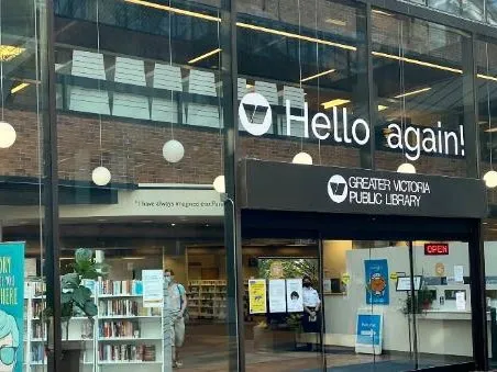 Exterior entrance of a library branch with 'Hello again!' and 'Greater Victoria Public Library' signage