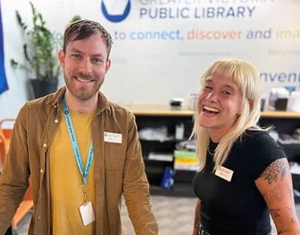 Two library staff members smiling behind a service desk