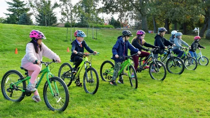 Students lined up on their bicycles on a grassy hill preparing for a race