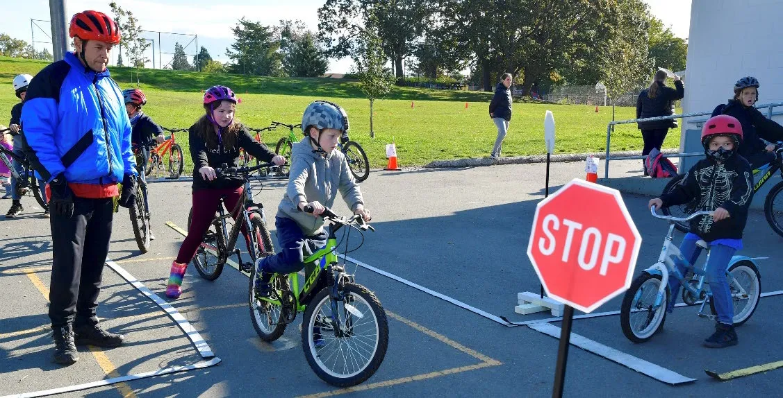 An instructor in a blue jacket teaching students about traffic signs at a simulated stop sign