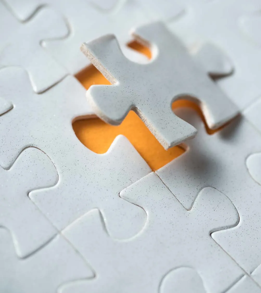 Close-up of white jigsaw puzzle pieces with one piece lifted to reveal an orange background