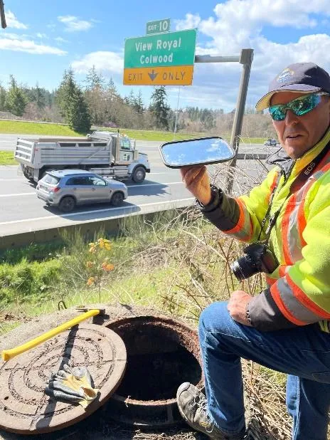 Photo of an Engineering Technologist using a mirror to inspect a sewer manhole at Erskine Lane