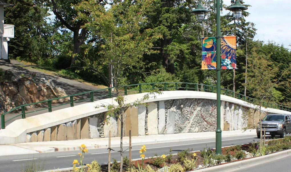 Photo of a public art installation featuring a stone mosaic wall and decorative banners alongside a road