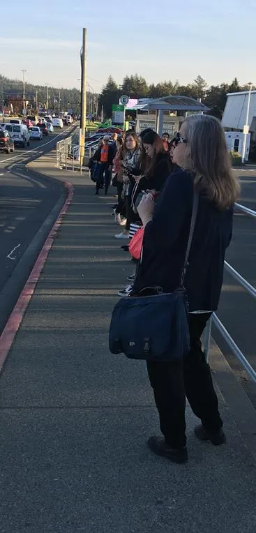 Photo of people waiting for a bus along a sidewalk.