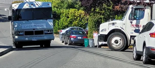 View showing a garbage truck and a service truck stopped on Jedburgh Road due to a parked motorhome and other vehicles