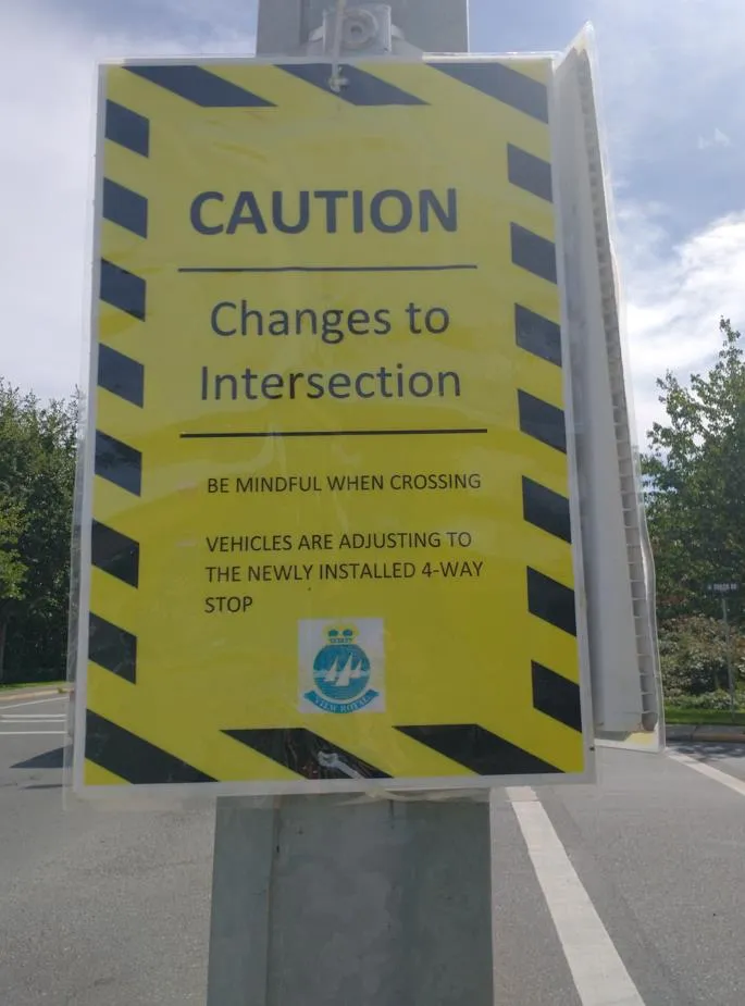 Yellow caution sign with black striped borders detailing changes to the intersection and a newly installed 4-way stop