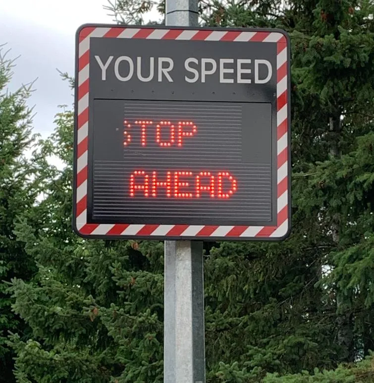 A close-up of a digital radar sign with "YOUR SPEED" at the top and "STOP AHEAD" displayed in red LEDs.