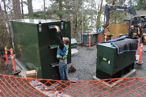 worker standing by the newly installed green electrical control kiosk and generator