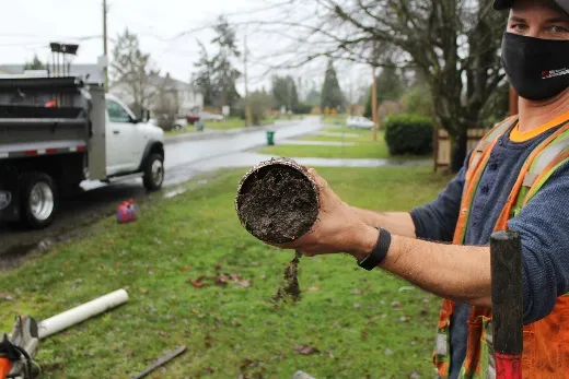worker holding a section of drainpipe completely blocked with dirt and debris