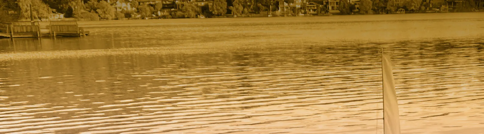 A wide view of a lake with houses on the far shore and a toy sailboat in the foreground