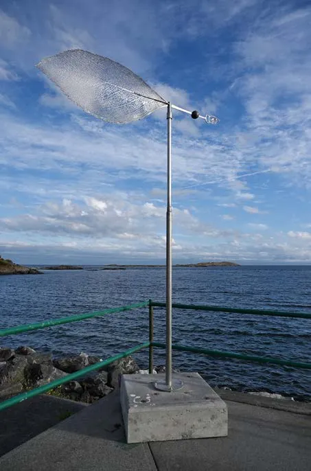 Kinetic metal sculpture resembling a leaf or sail by the ocean