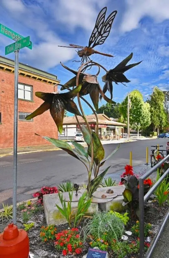 Metal sculpture of flowers with a dragonfly in a landscaped area