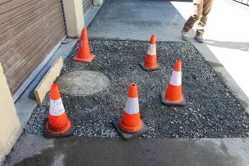 Sewer manhole raised to surface level and surrounded by gravel and traffic cones