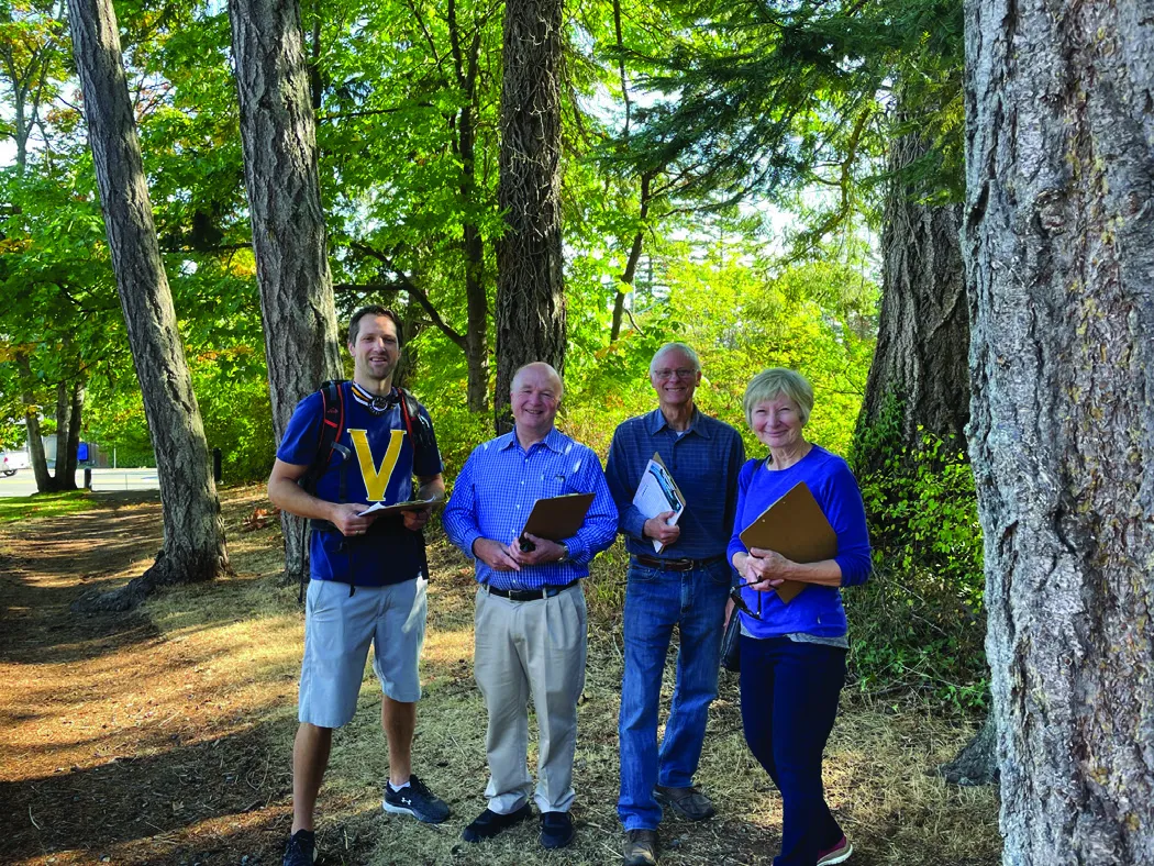 Four community members standing in a forest setting, holding clipboards and smiling.