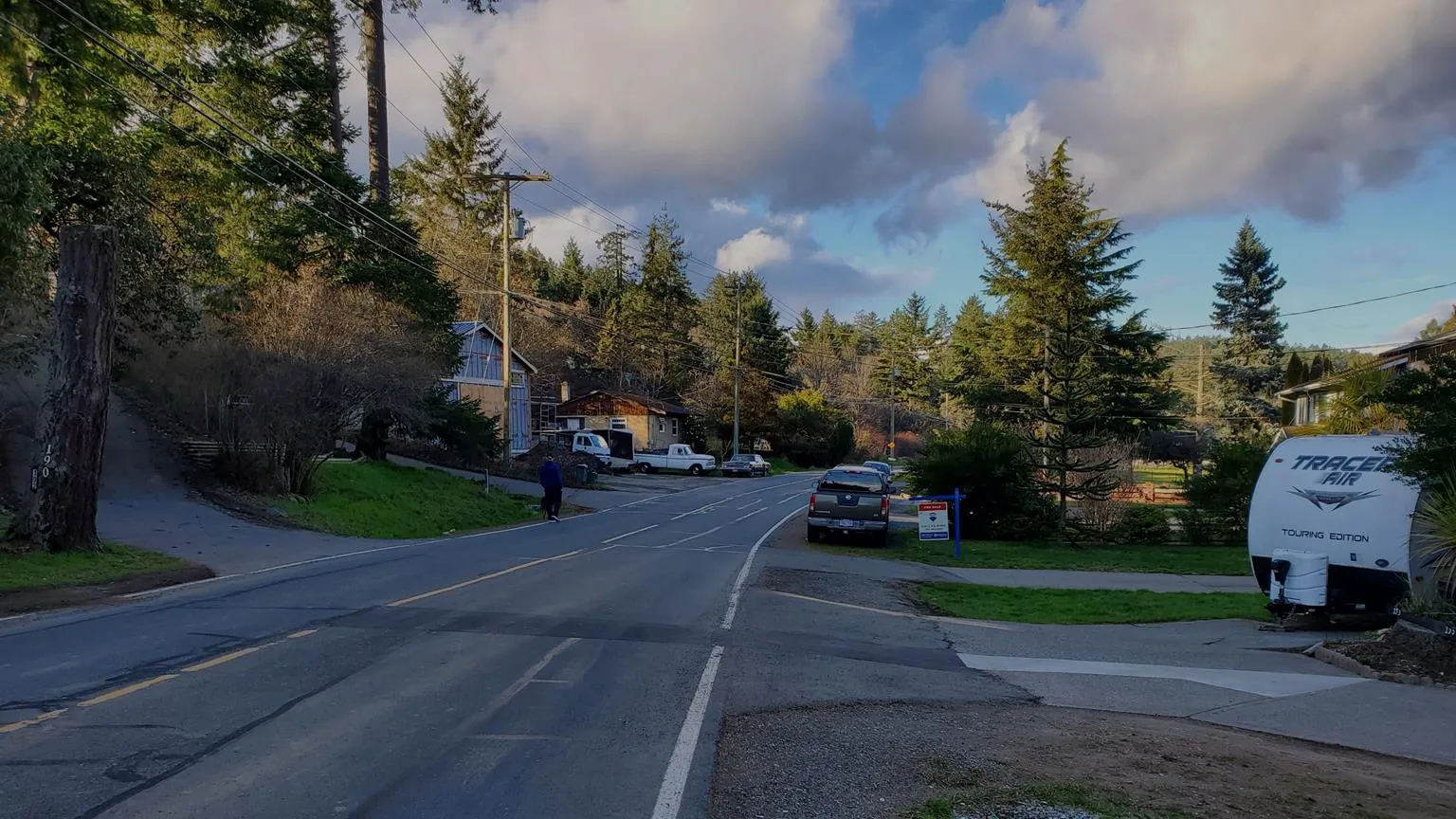 Street view of Atkins Road showing a lack of sidewalks and vehicles parked along the paved edge
