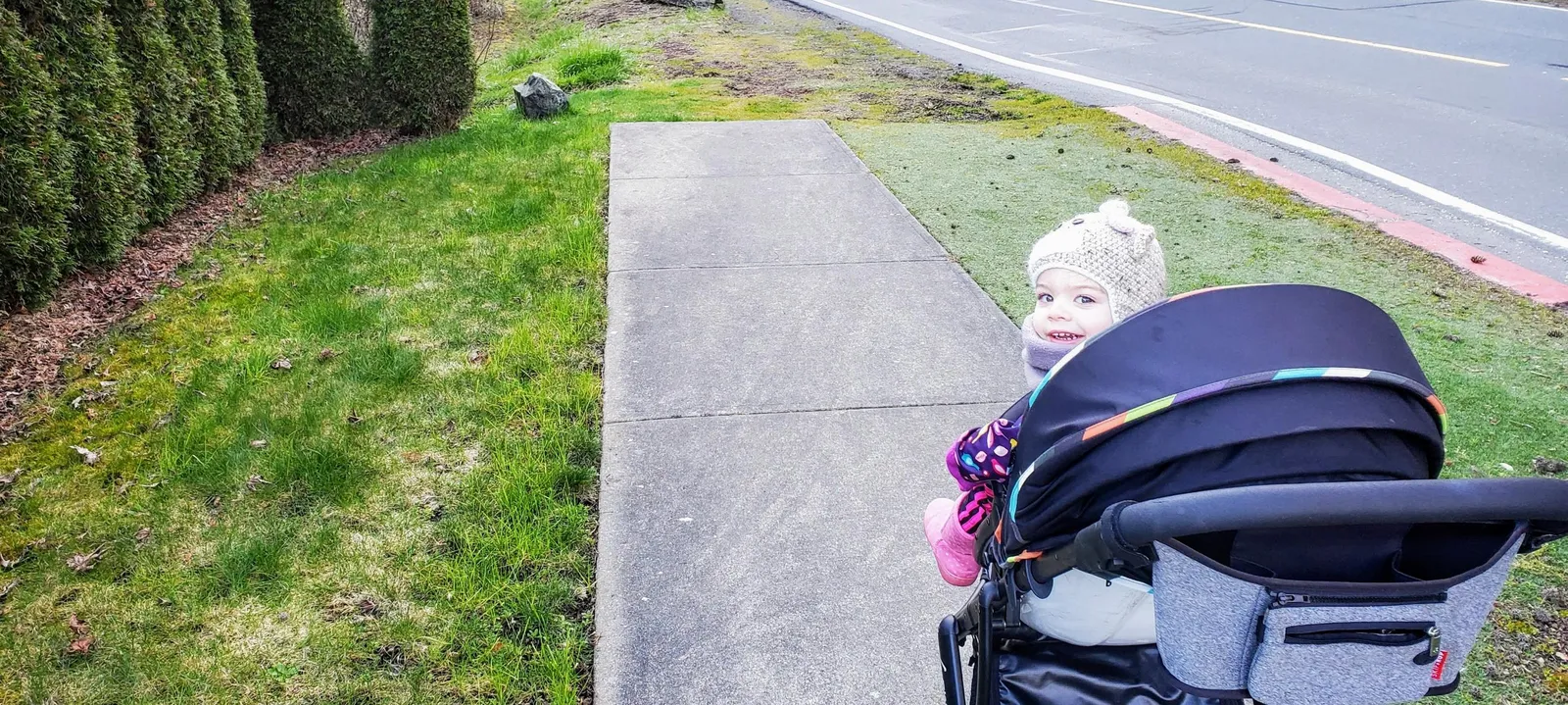 A concrete sidewalk on Atkins Road that terminates into a grassy area, shown with a child in a stroller